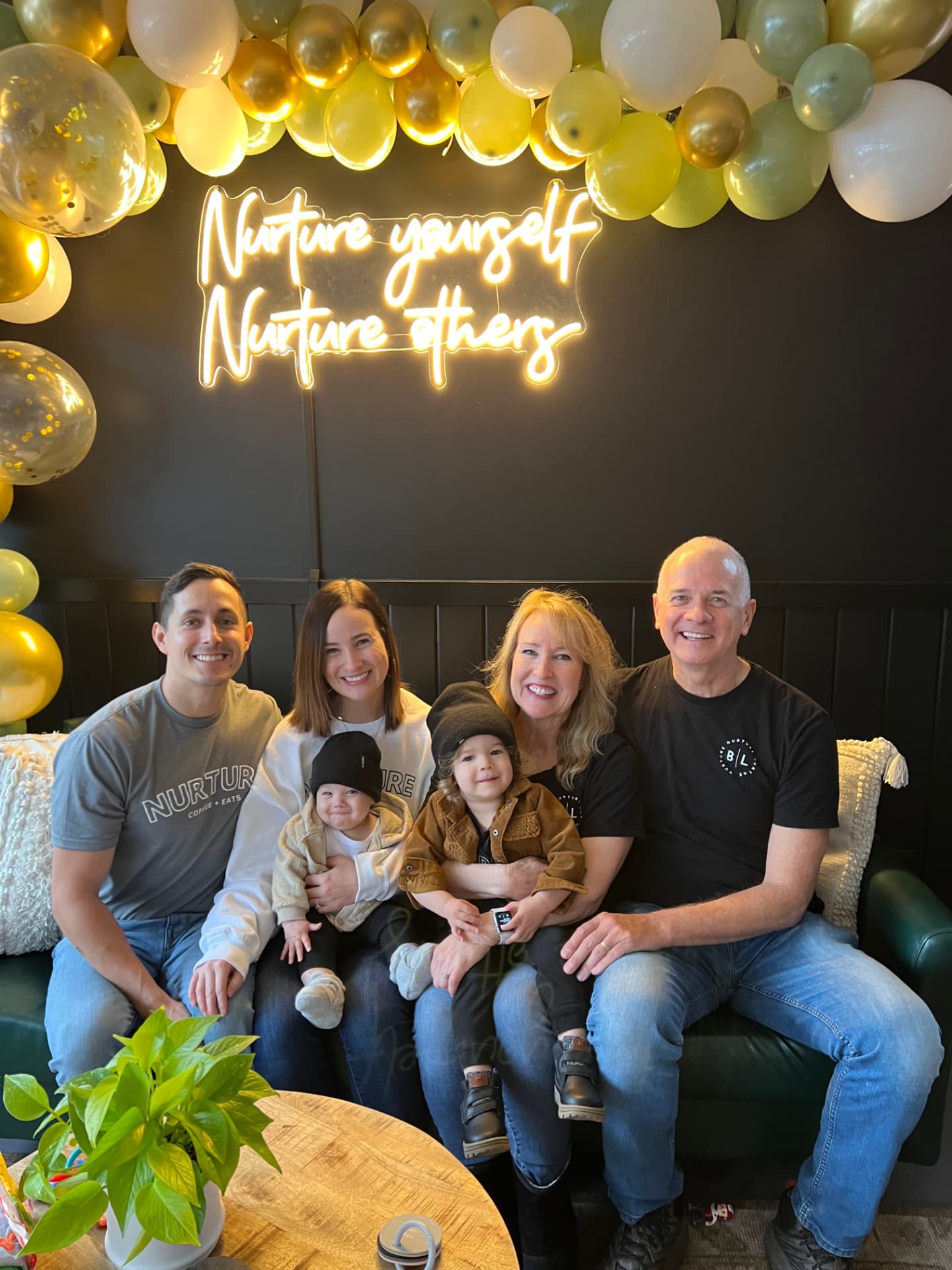 The Nurture family on the green couch under the neon Nurture yourself, Nurture others sign